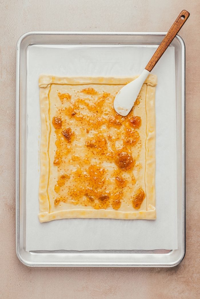 Puff pastry rolled out on a baking sheet with the edges turned in to make a crust and fig jam brushed over it.