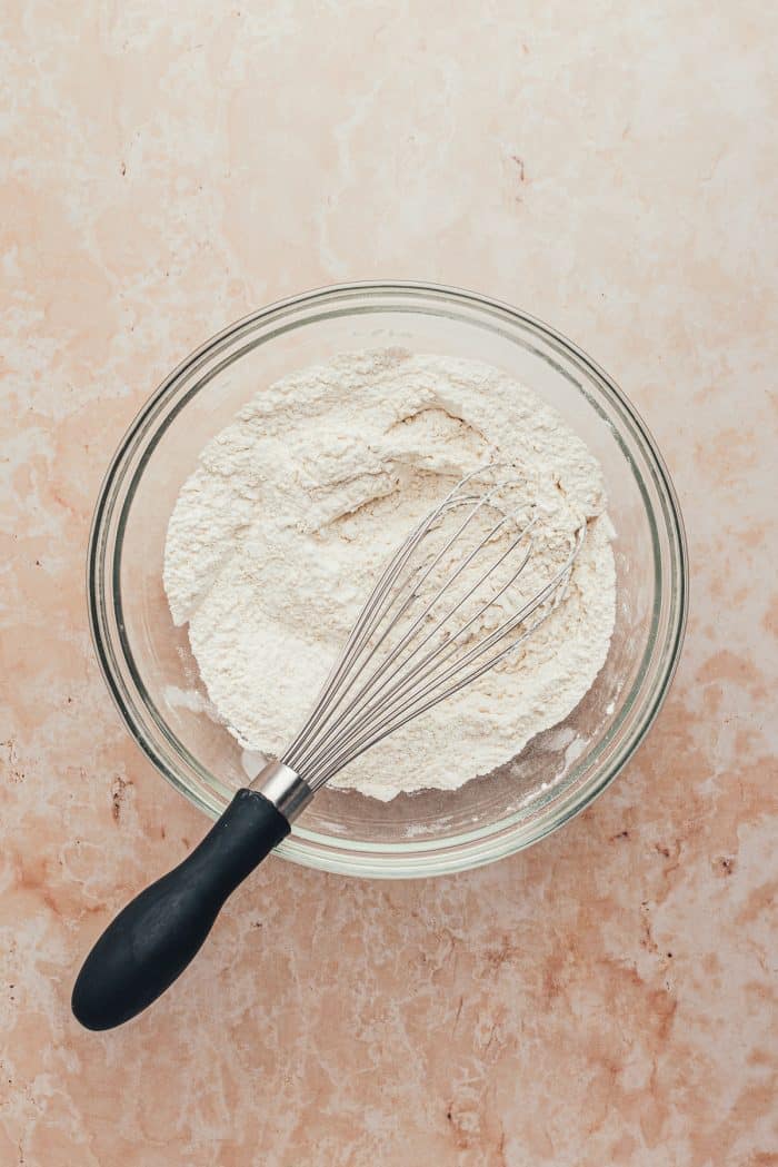 A glass bowl with flour and a whisk.