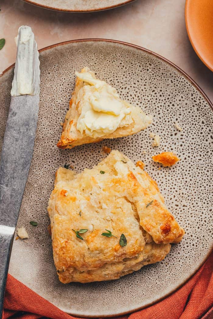 A plate with a scone cut in half with butter smeared on one piece.