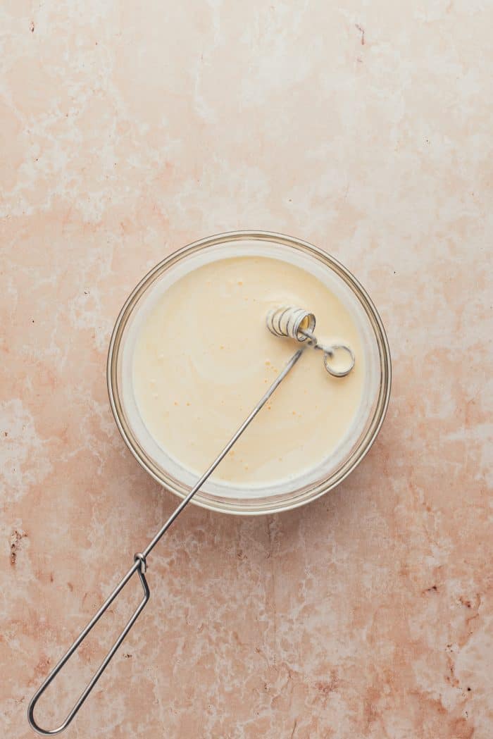 A glass bowl with heavy cream and an egg mixed together.