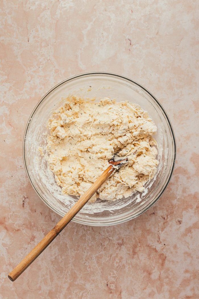 A glass bowl with the wet and dry ingredients mixed together with a wooden spoon.