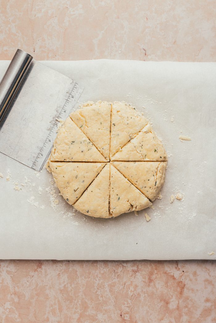 The scone dough in a disk shape, cut into scones on parchment paper.