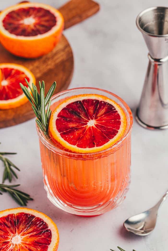 A blood orange mocktail with a slice of blood orange and a sprig of rosemary.