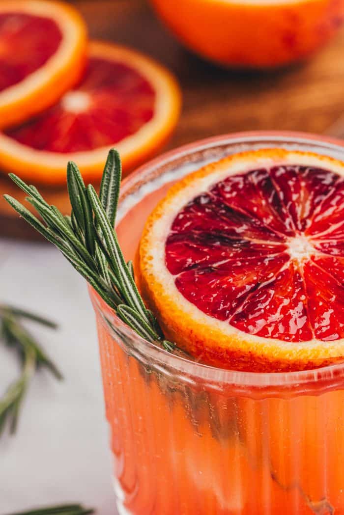 A blood orange mocktail with a slice of blood orange and a sprig of rosemary.