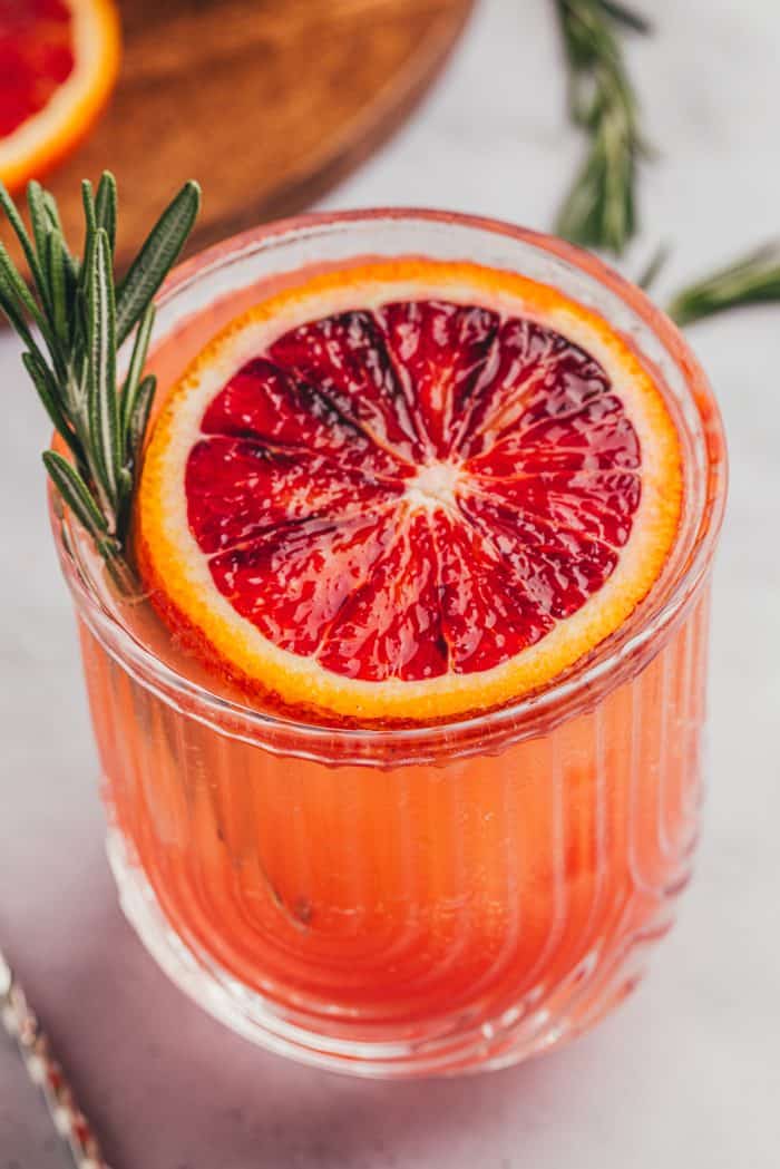 A blood orange mocktail with a slice of blood orange and a sprig of rosemary.