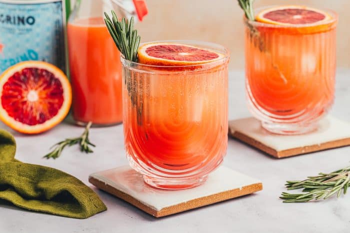 Three blood orange mocktails with slices of blood orange and sprigs of rosemary.