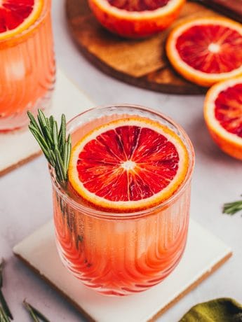 A blood orange mocktail with a slice of blood orange and a sprig of rosemary.