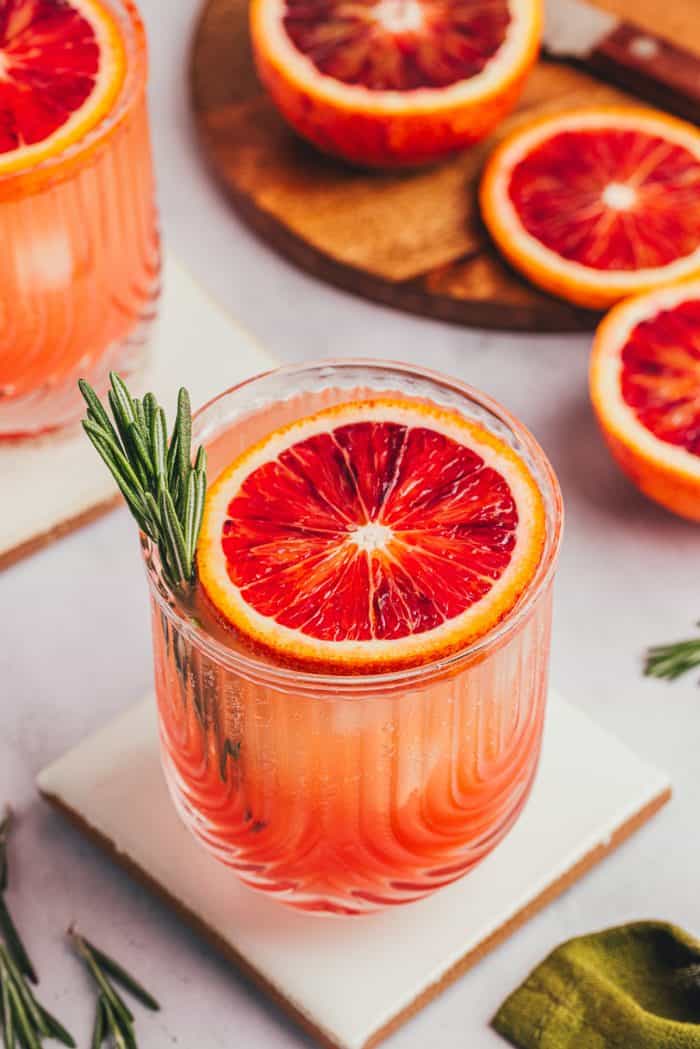 A blood orange mocktail with a slice of blood orange and a sprig of rosemary.