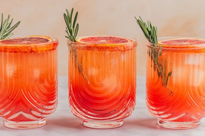 Three blood orange mocktails with slices of blood orange and sprigs of rosemary.