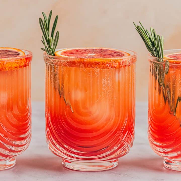 Three blood orange mocktails with slices of blood orange and sprigs of rosemary.