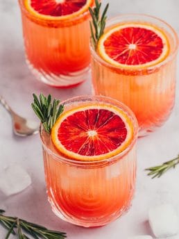 Three blood orange mocktails with slices of blood orange and sprigs of rosemary.