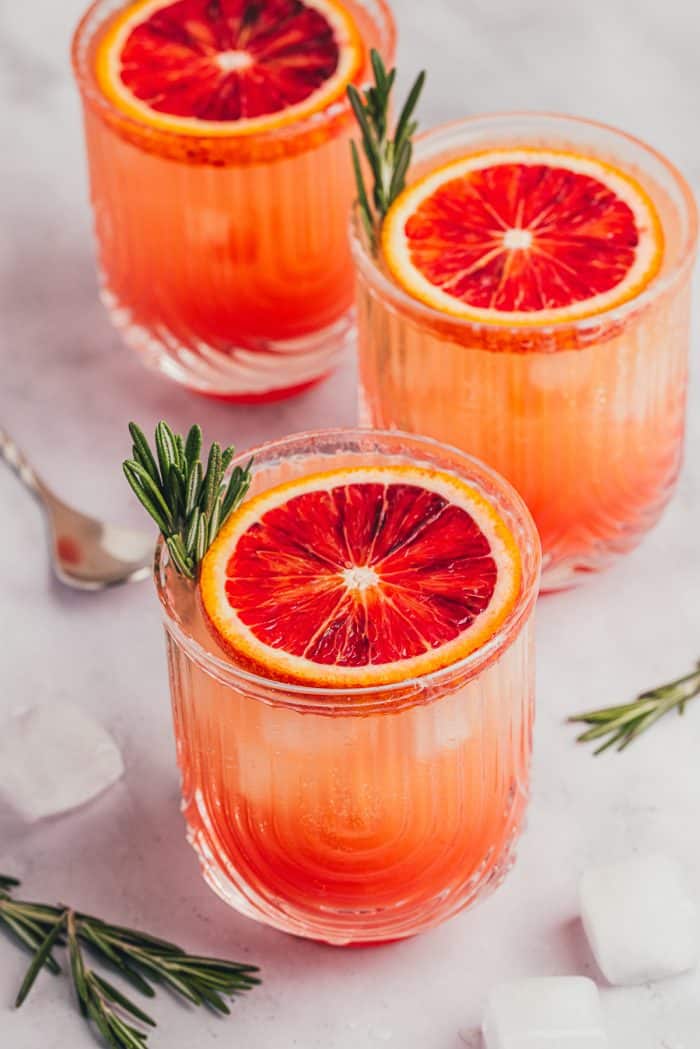 Three blood orange mocktails with slices of blood orange and sprigs of rosemary.