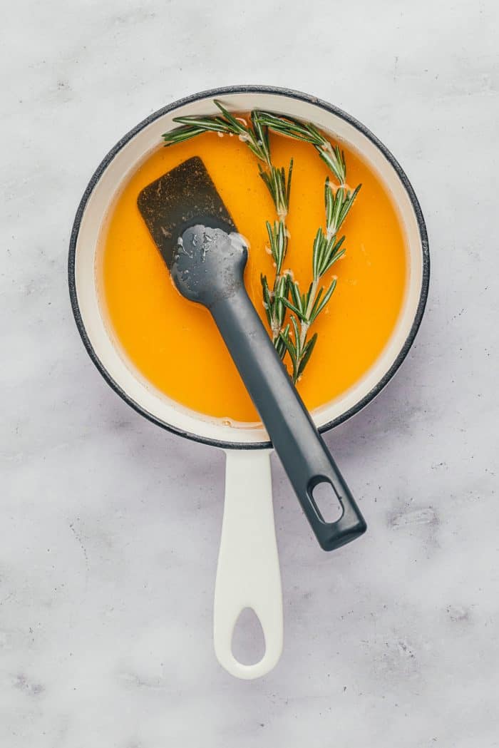 A saucepan with honey and rosemary sprigs.