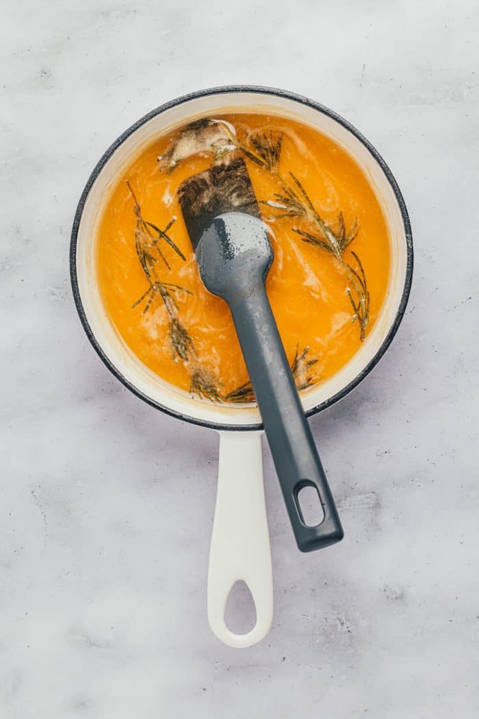 A saucepan with honey and rosemary sprigs.