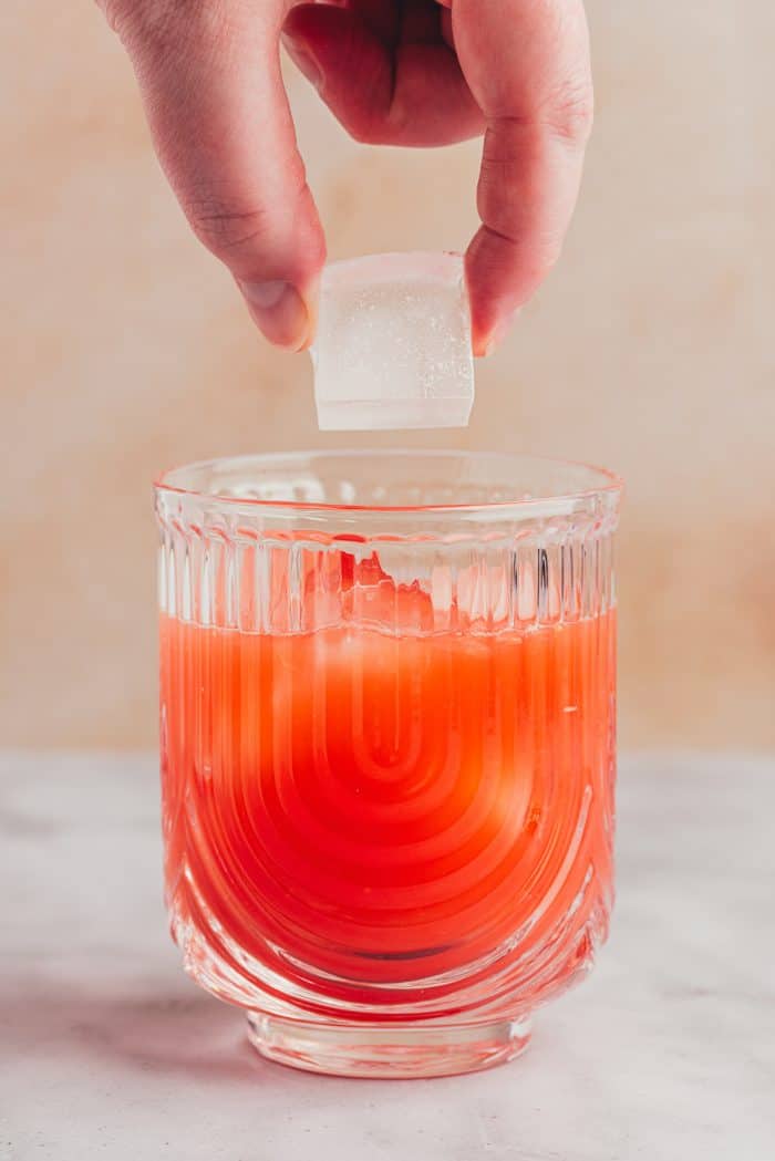 Ice cubes being added to a glass with a blood orange mixture.