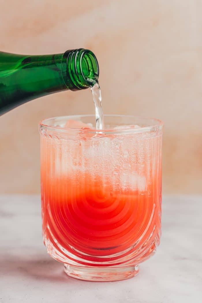 Sprinkling water being added to a glass with a blood orange mixture.