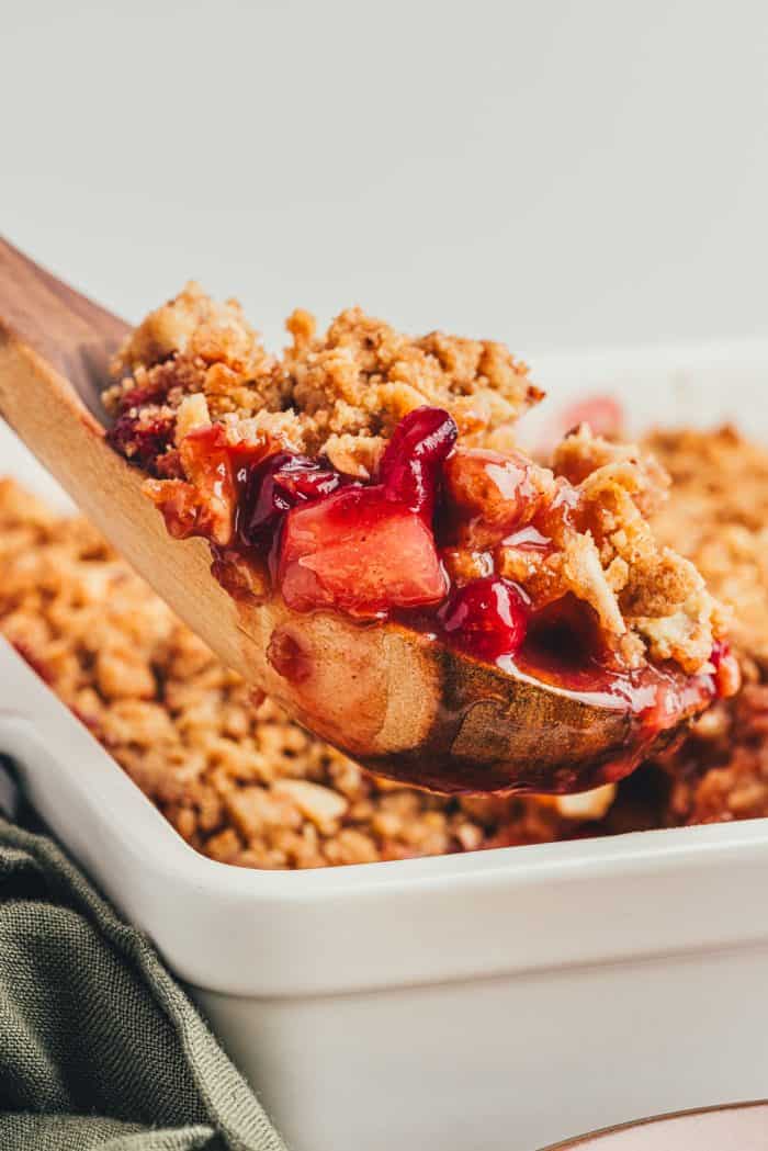 A scoop of pear cranberry crumble that is being scooped out with a large spoon.