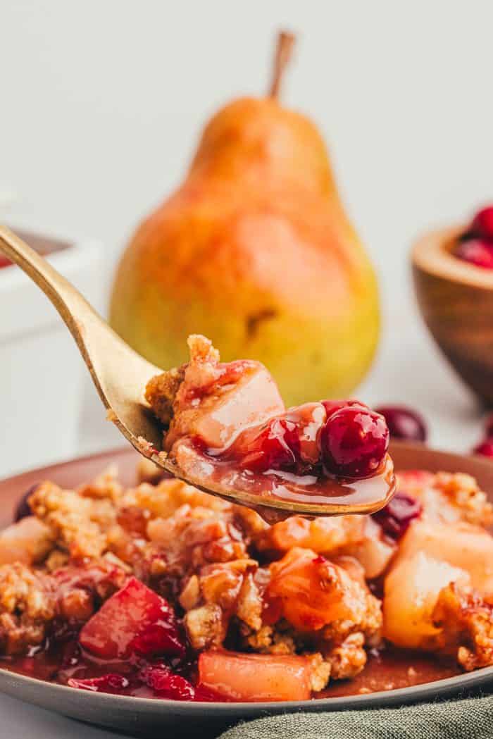 A red plate with a scoop of cranberry pear crumble with ice cream that is melting and a golden spoon.