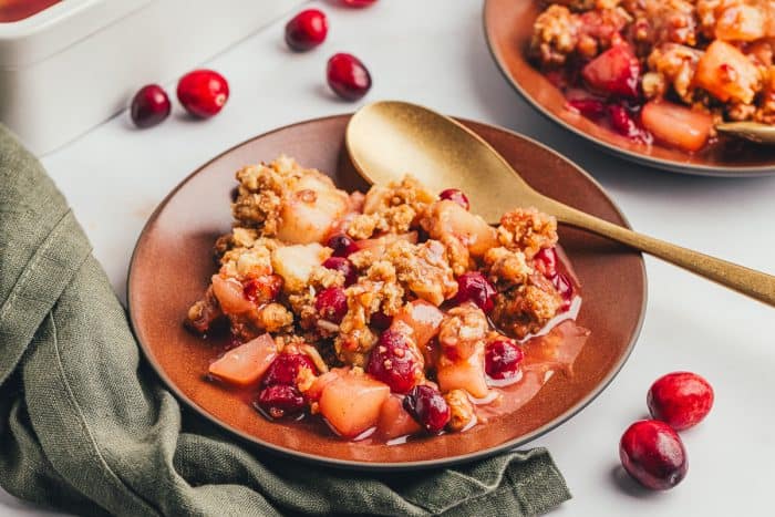 A red plate with a scoop of cranberry pear crumble with a golden spoon.