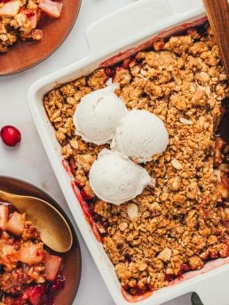 An overhead view of a square white baking dish with cranberry pear crumble with a couple scopes of vanilla ice cream.