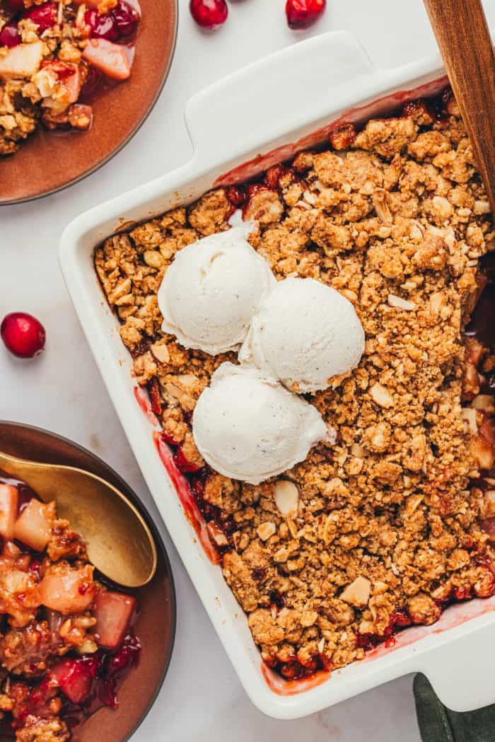 An overhead view of a square white baking dish with cranberry pear crumble with a couple scopes of vanilla ice cream.