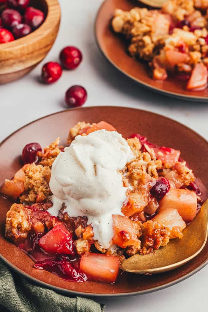 A red plate with a scoop of cranberry pear crumble with ice cream that is melting and a golden spoon.