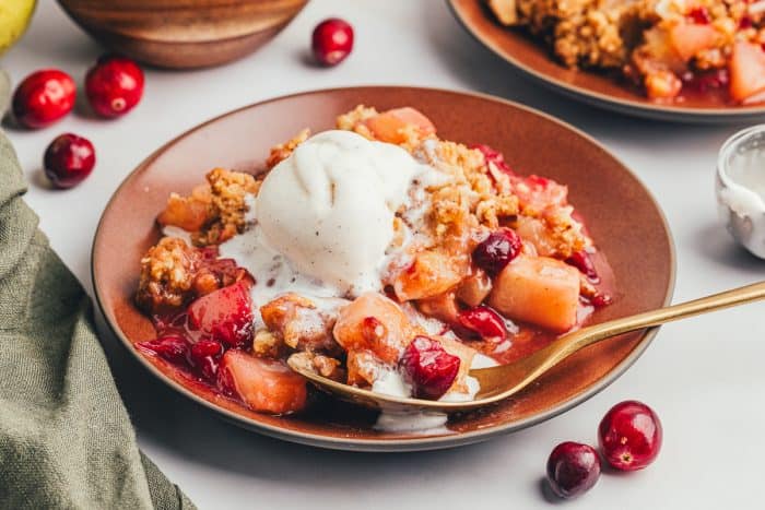 A red plate with a scoop of cranberry pear crumble with ice cream that is melting and a golden spoon.