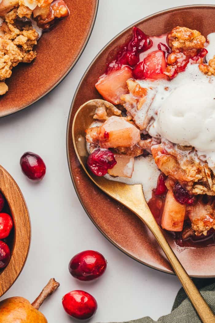 A red plate with a scoop of cranberry pear crumble with ice cream that is melting and a golden spoon.