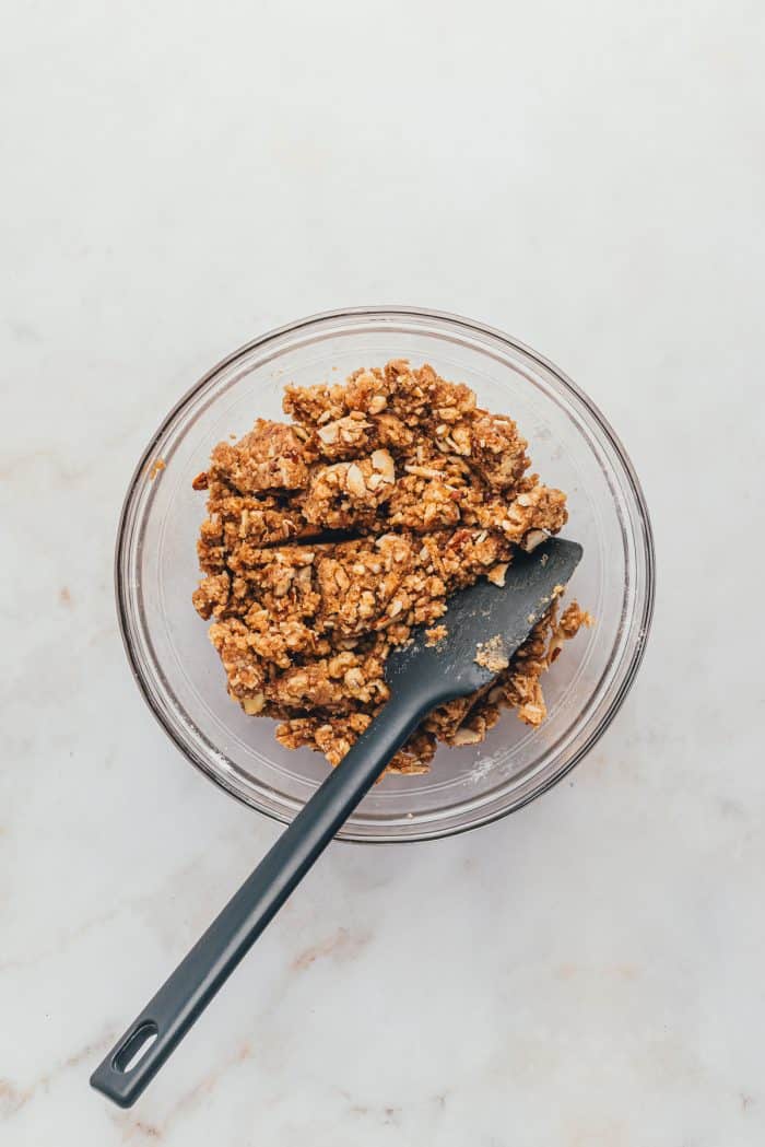 A glass bowl with the crumble topping with a spatula.