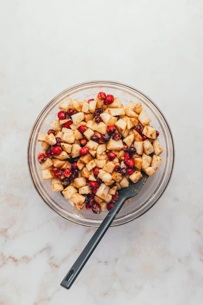 A glass bowl of the pear and cranberry filling with a spoon.