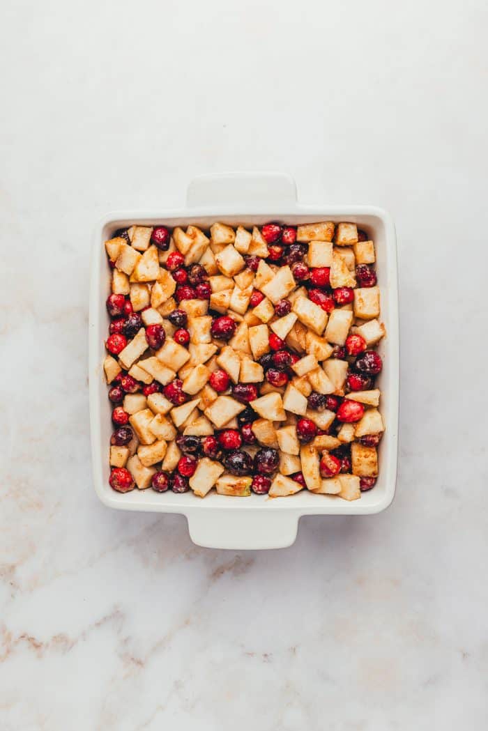 A white square dish with the cranberry pear crumble filling in it.