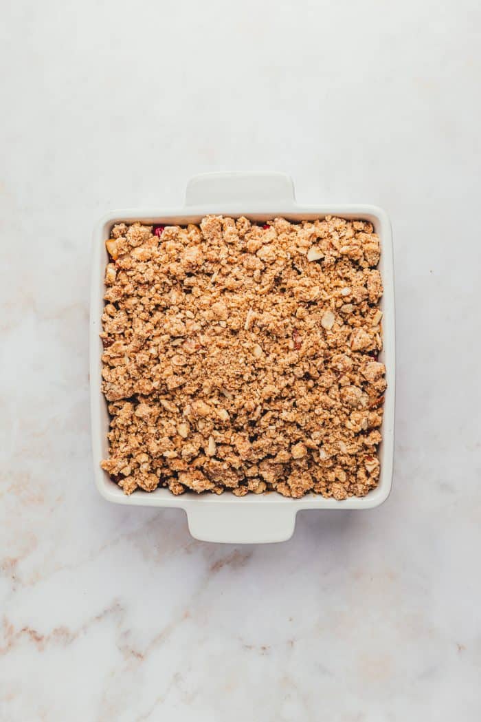 A white dish with an unbaked cranberry pear crumble.