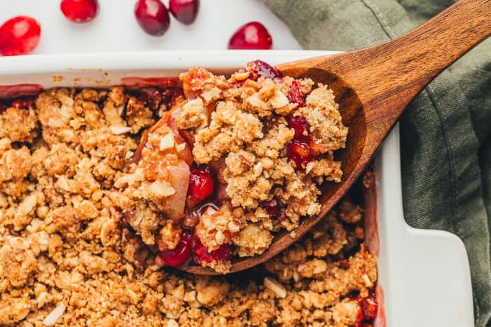 A scoop of pear cranberry crumble that is being scooped out with a large spoon.