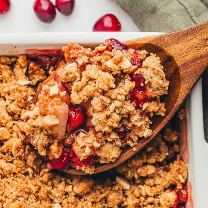 A scoop of pear cranberry crumble that is being scooped out with a large spoon.