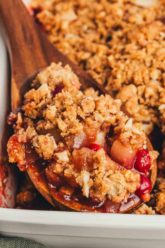 A scoop of pear cranberry crumble that is being scooped out with a large spoon.