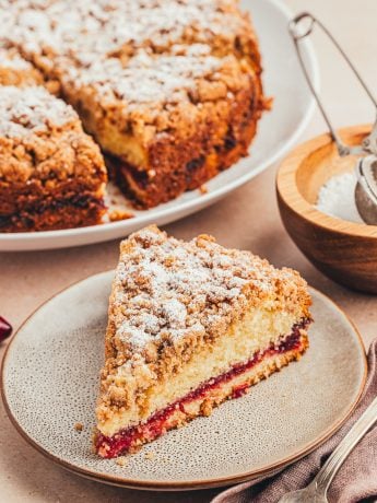 A plate with a slice of coffee cake and the whole cake in the background.