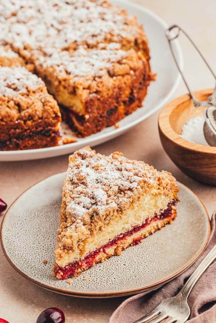 A plate with a slice of coffee cake and the whole cake in the background.