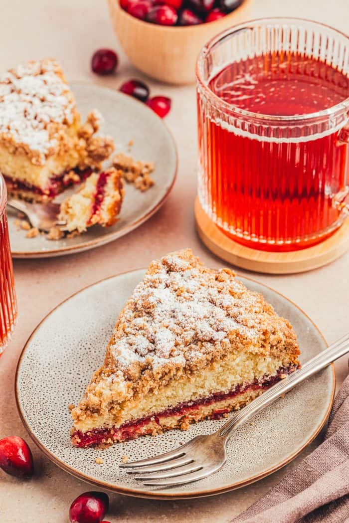 A plate with a slice of cranberry coffee cake with a fork and a glass of a red drink.