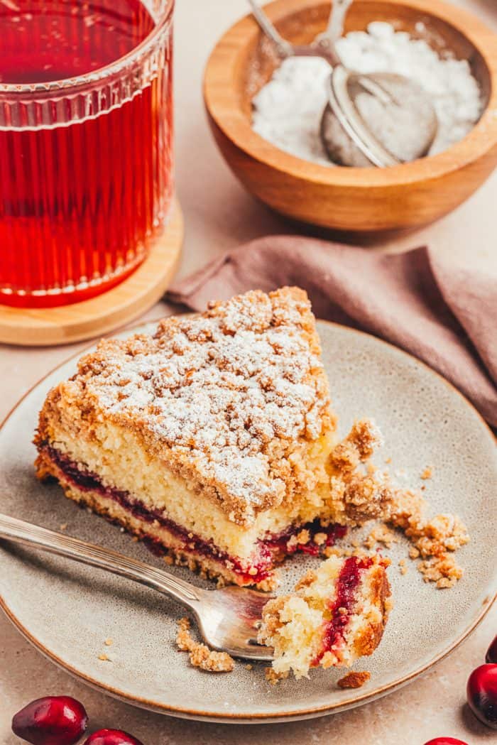 A plate with a slice of coffee cake with a swirl of cranberry jam and a bite taken out of the cake.