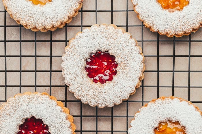 A cooling rack with Linzer cookies with powdered sugar and jam.