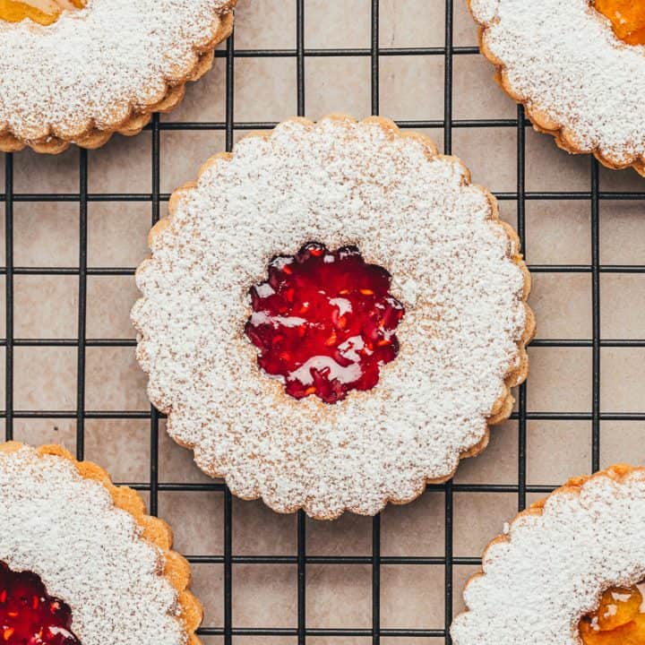 A cooling rack with Linzer cookies with powdered sugar and jam.