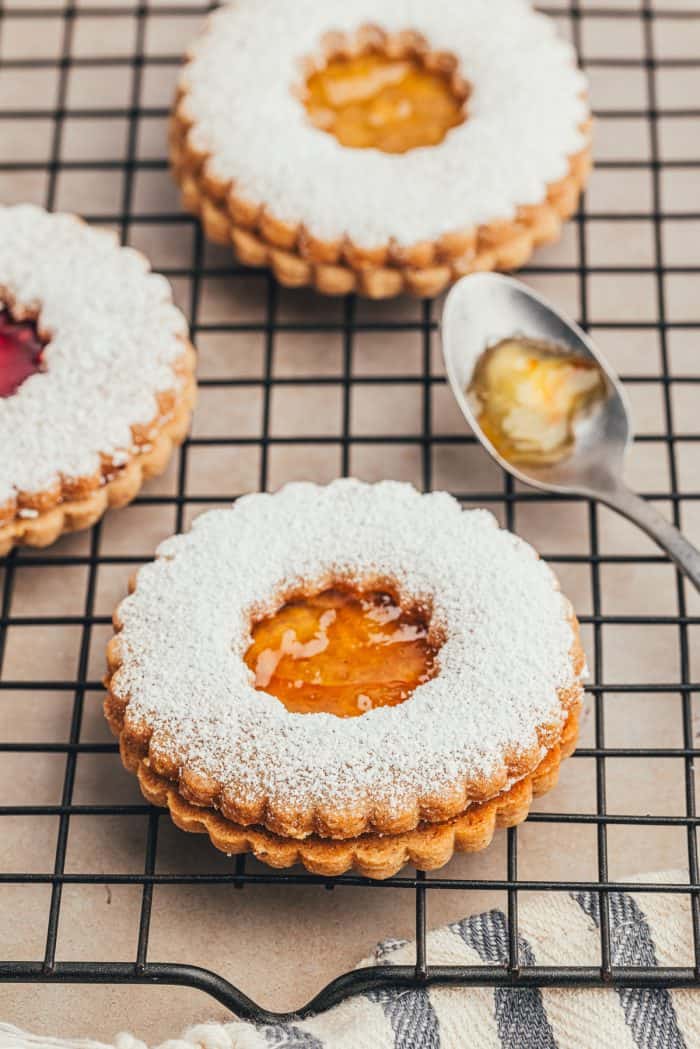 A cooling rack with baked Linzer cookies and a spoon with jam.