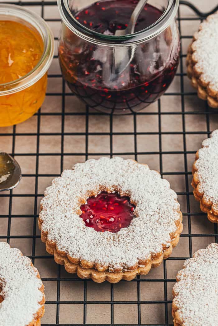 A cooling rack with hazelnut Linzer cookies and glass bowls of jam.