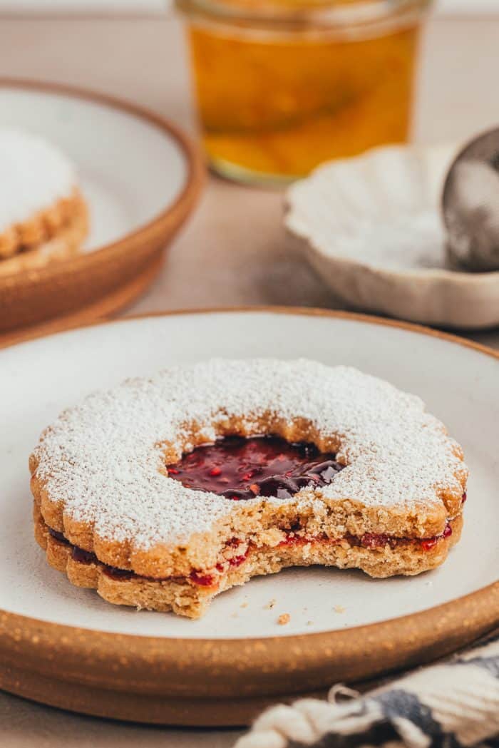 A plate with a hazelnut Linzer cookie with a bite taken out of it.