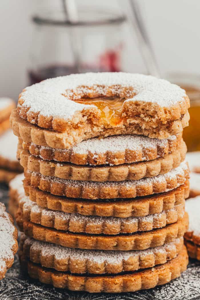 A stack of Linzer cookies with one cookie that has a bite taken out of it.