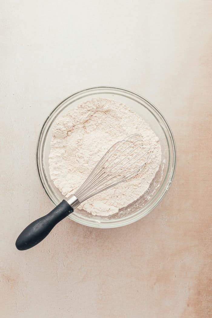 A glass bowl with flour and a whisk.