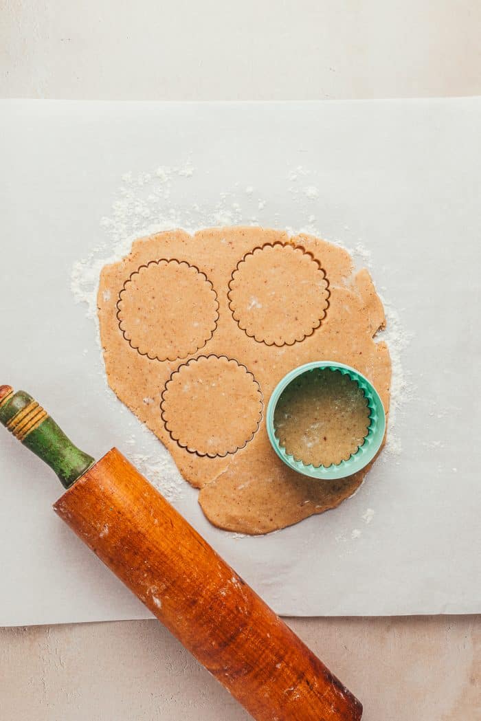 Cookie dough rolled out on parchment paper with a cookie cutter and a rolling pin.