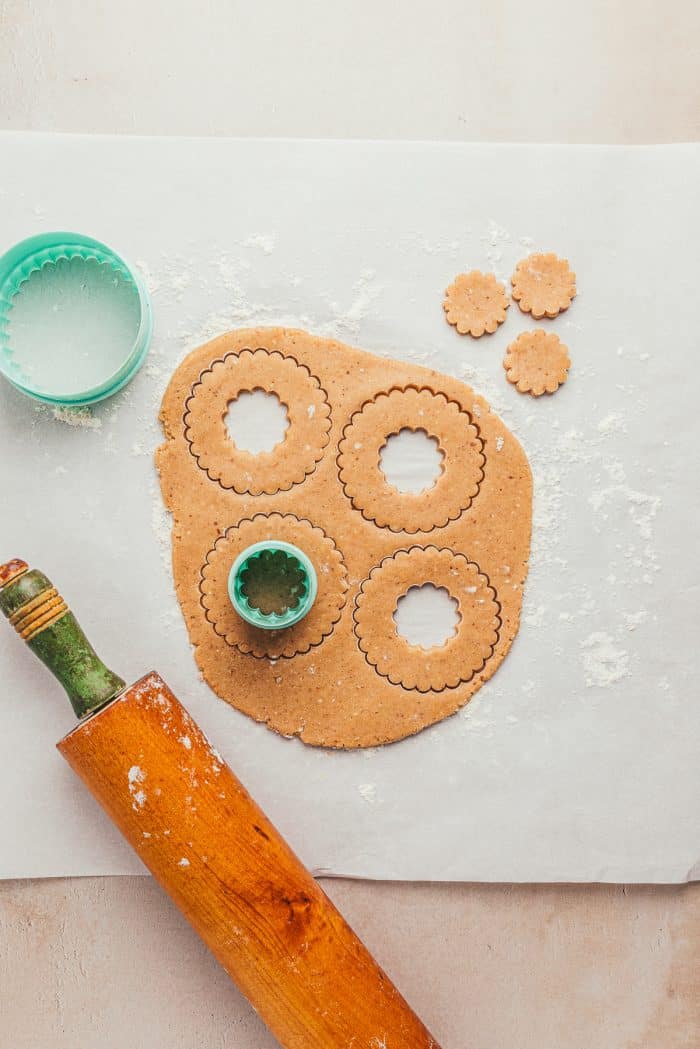 Parchment paper with Linzer dough with cookie cutters and a rolling pin.