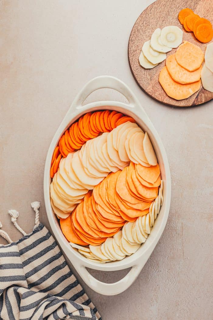 A variety of sliced root vegetables in a white baking dish.