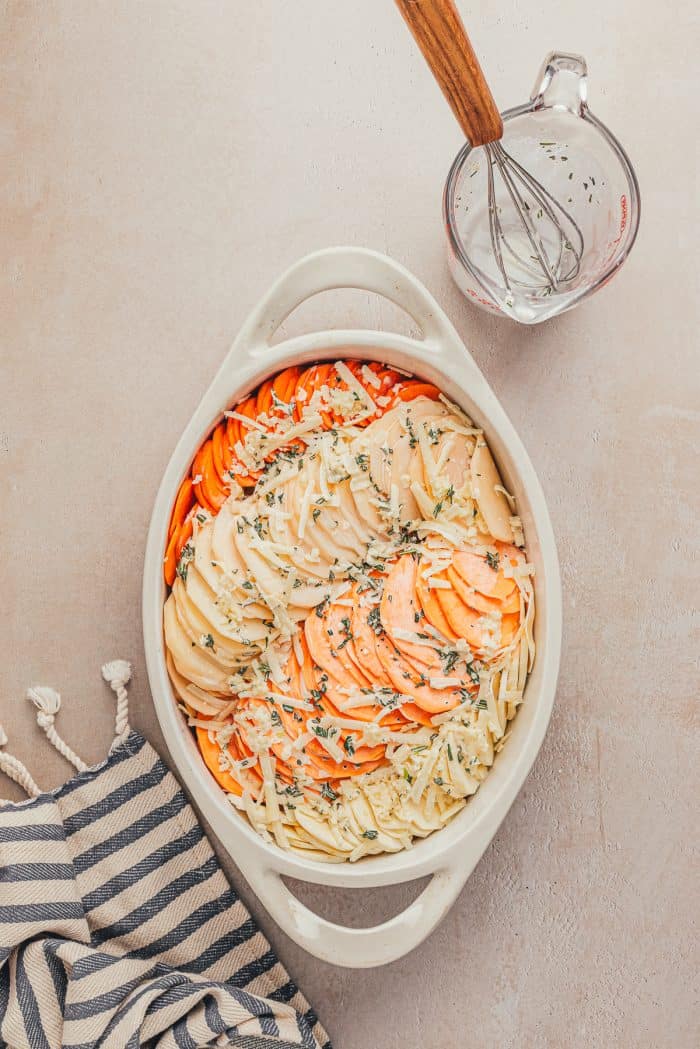 A variety of sliced root vegetables in a white baking dish.